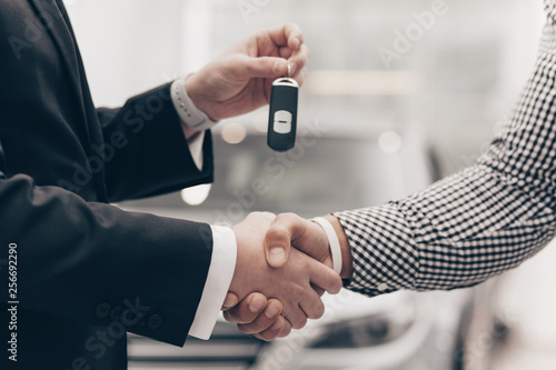 Cropped close up shot of a man shaking hands with car salesman at the dealership. Car dealer handing automobile keys to his male customer, after selling him an auto. Handshake, rental, deal concept