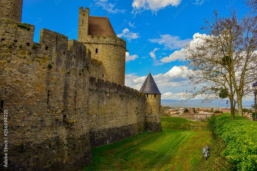 se ven las murallas de un castillos con sus torres y al fondo la ciudad