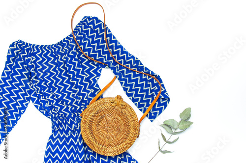 Stylish trendy feminine summer clothing blue dress jumpsuit, round rattan bag sprig eucalyptus on white background Trendy hipster look Female fashion background blog concept Flat lay top view
