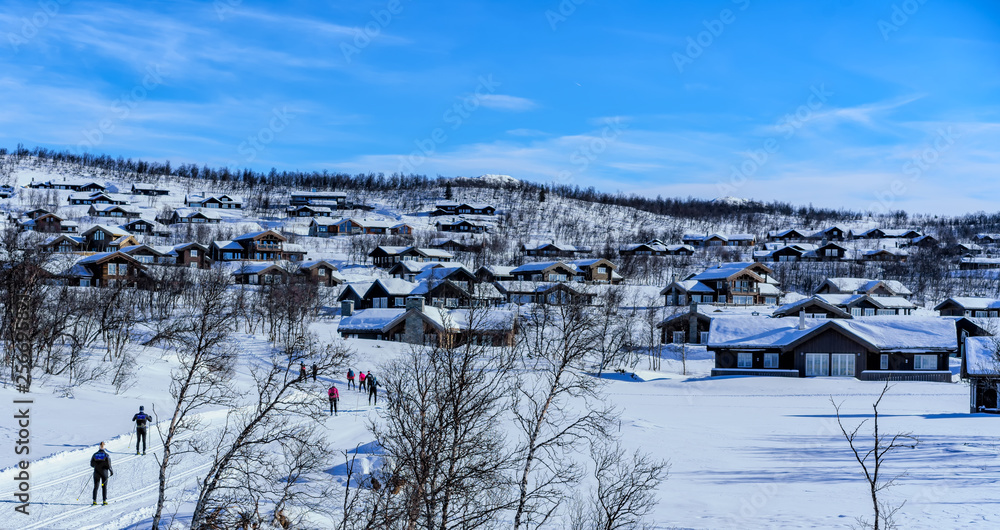 People on ski trails pass wooden houses in Beitostolen on the high mountain area of jotunheimen, Norway