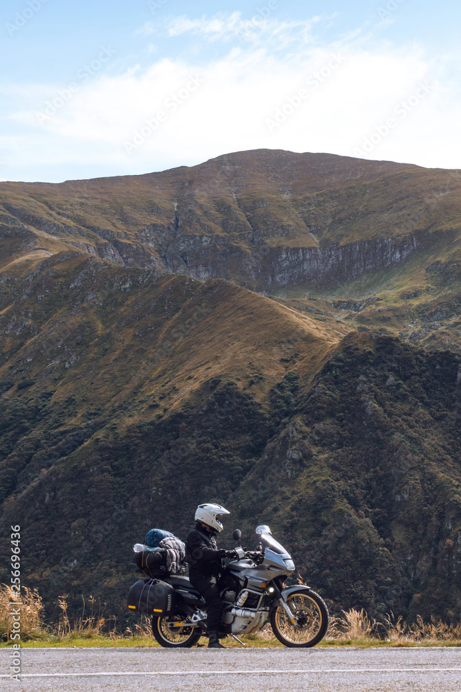 Biker is sitting on his adventure motorcycle, the top mountain in background, enduro, beautiful view, danger road in mountains, freedom, extreme vacation. Transfagarasan Romania, vertical photo