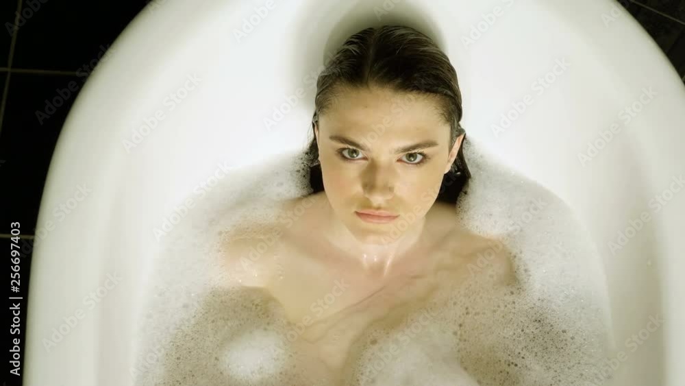 Top view of young brunette woman taking a bubble bath in bathtub. She dipping her head in the water and looking at camera. 4K Top view of young brunette woman taking a bubble bath in bathtub. She dipping her head in the water and looking at camera. 4K