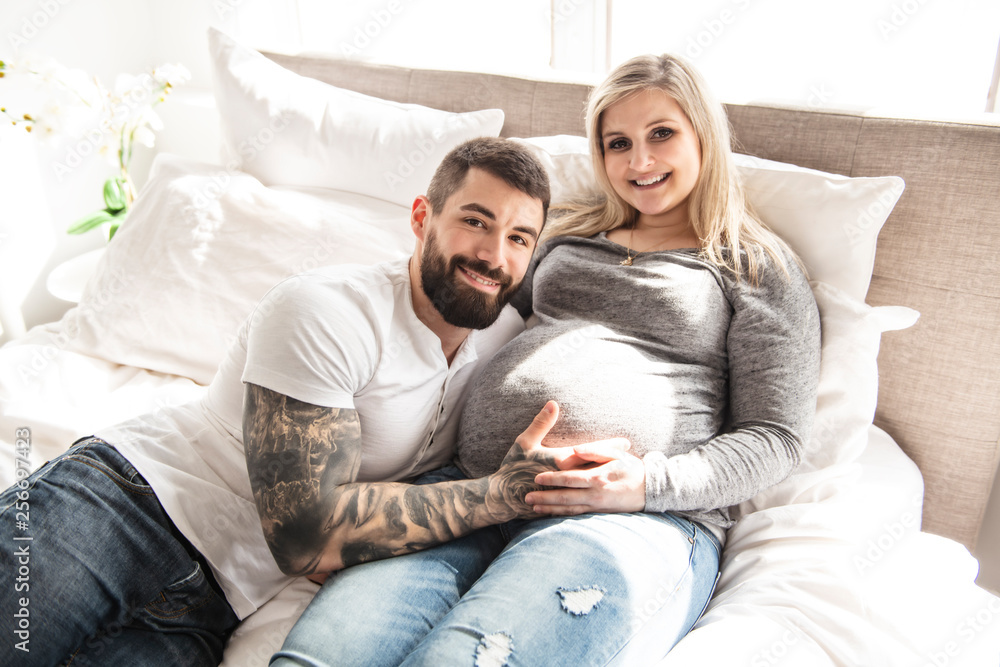 the man leaned against to the baby bump of his pregnant wife, who is lying on the bed the man leaned against to the baby bump of his pregnant wife, who is lying on the bed