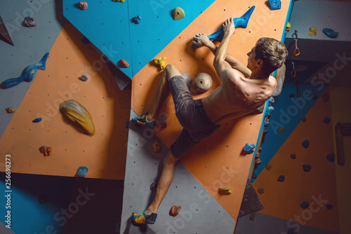 Workout exercise. top view of a man climber climbs indoors in bouldering gym. Athletic man climbing up on practice wall - Image