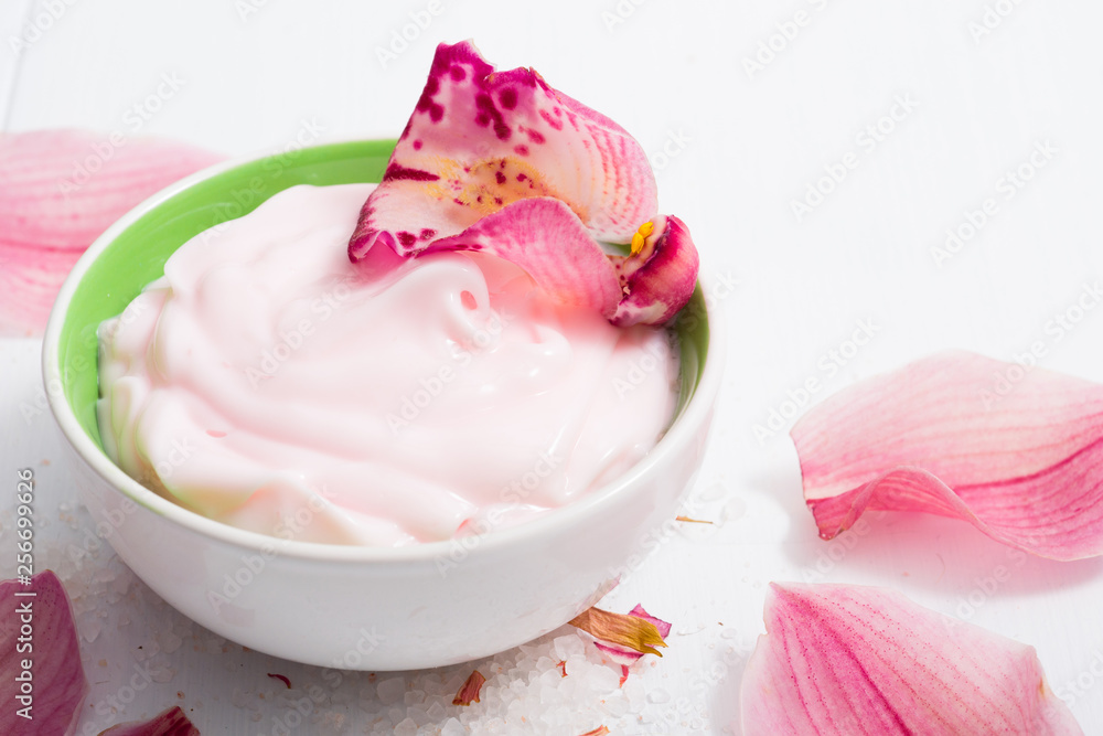 cosmetic cream with pink flower petals, white wood table cosmetic cream with pink flower petals, white wood table