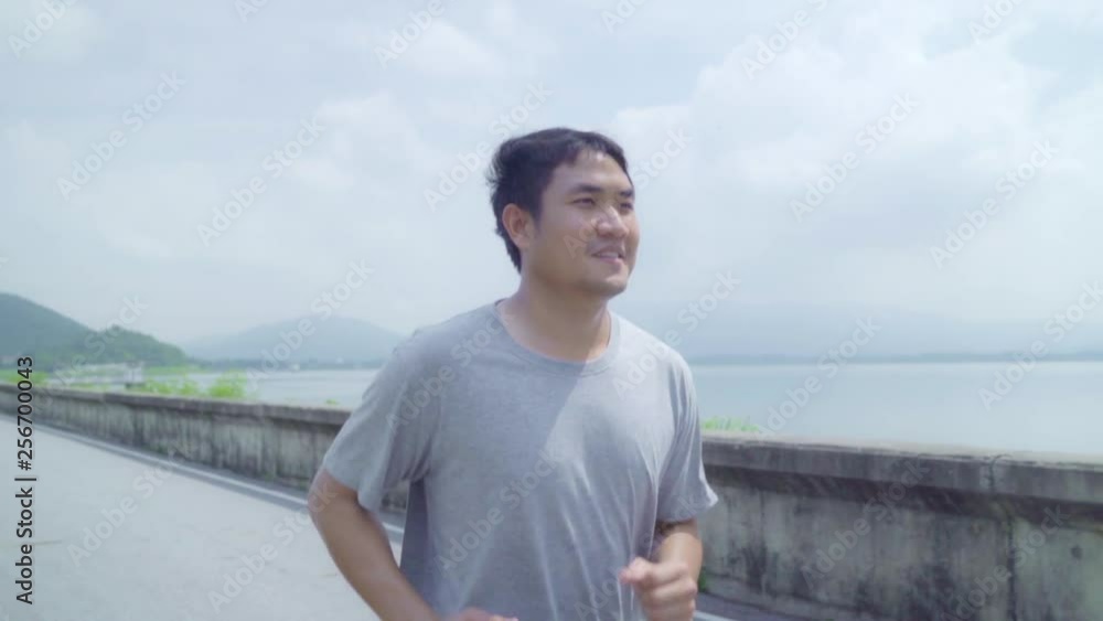 Slow motion - Asian runner man running and jogging on street, Healthy handsome young sporty male exercise near lake. Lifestyle fit and active men exercise on street concept. Slow motion - Asian runner man running and jogging on street, Healthy handsome young sporty male exercise near lake. Lifestyle fit and active men exercise on street concept.