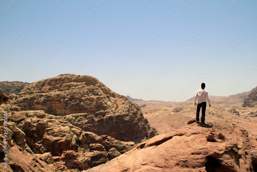 Young man on top of a peak looking over a valley in the rugged landscape of Petra, Jordan