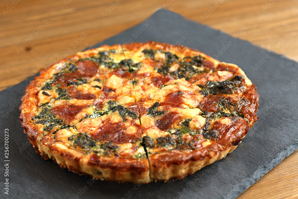 Italian traditional rustic quiche pizza with cheese, spinach  and tomatoes on a black plate in restaurante