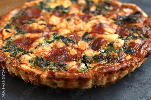 Italian traditional rustic quiche pizza with cheese  spinach  and tomatoes on a black plate in restaurant