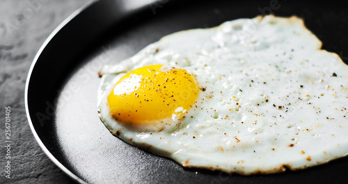 Fried egg in a iron frying pan on Dark grey black slate background