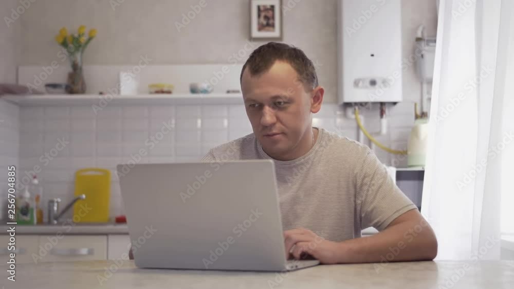 man working on a laptop at home in the kitchen, typing on a keyboard