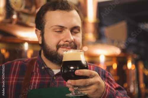 Close up of a happy male brewer smiling with his eyes closed, enjoying smelling delicious dark beer, copy space. Professional beermaker enjoying his tasty craft beer. Relax, leisure, weekend concept