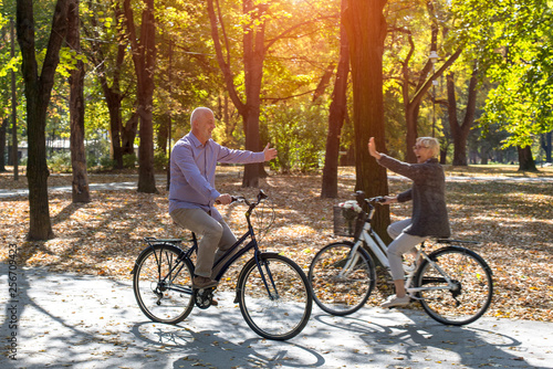 Senior man and woman enjoying spending time together while riding a bike in autumn park
