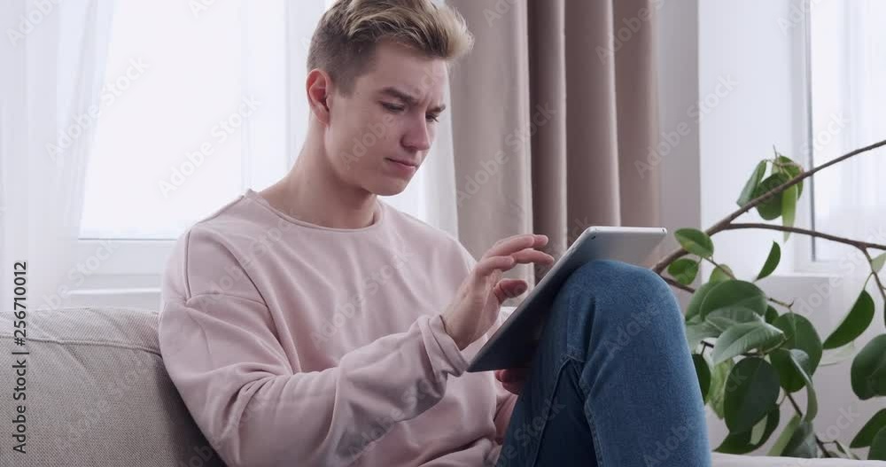 Handsome young man using digital tablet on sofa at home Handsome young man using digital tablet on sofa at home