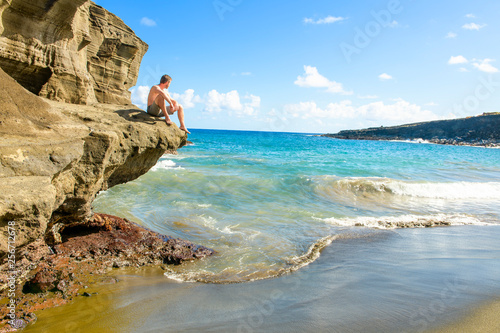 Tourist sit on rock of the beautiful Green Sand Beach, Big Island, Hawaii