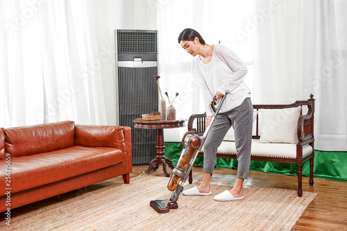 Asian teenage girl using a wireless vacuum cleaner to clean the carpet in the living room in the living room © jeson