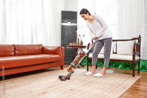 Asian teenage girl using a wireless vacuum cleaner to clean the carpet in the living room in the living room