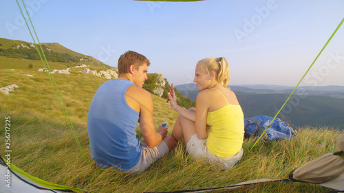 CLOSE UP: Girl shows her phone to her annoyed boyfriend and he waves at her. photo