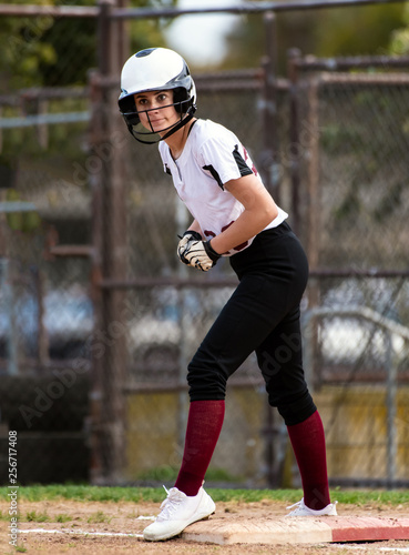 Female teen softball player in black and white uniform showing wide eyes inside her helmet while on first base.