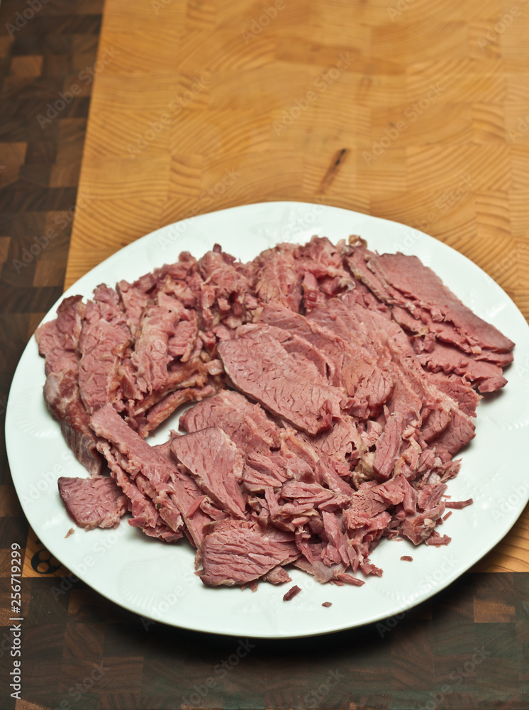 Top view, medium distance, three pound, raw, corn beef brisket, cooked and sliced on a white, round plate on bamboo, wood, cutting board, ingredients for, St patrick's day dinner Top view, medium distance, three pound, raw, corn beef brisket, cooked and sliced on a white, round plate on bamboo, wood, cutting board, ingredients for, St patrick's day dinner