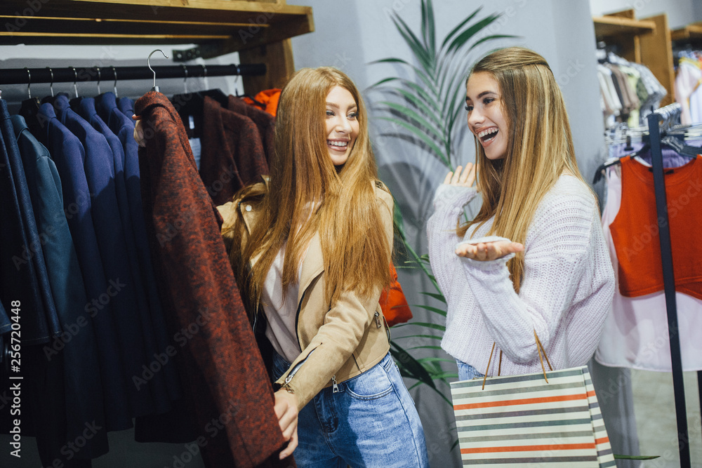 Fototapeta premium Grls with gift bags are choosing coat and smiling while doing shopping in the mall.