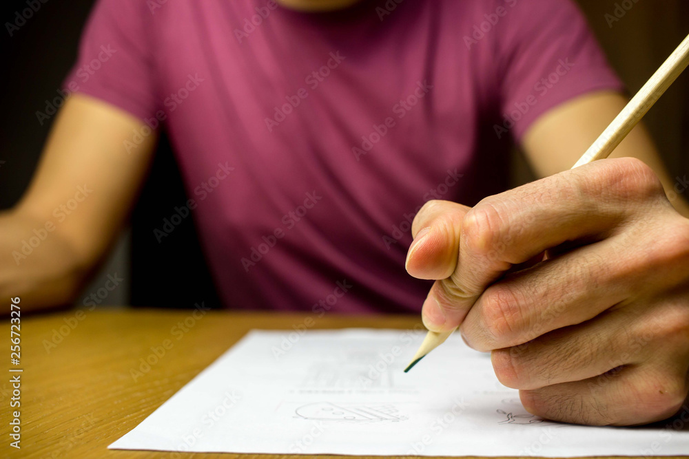 College student writing on a paper his notes for the exam. Close-up on the pencil College student writing on a paper his notes for the exam. Close-up on the pencil