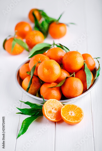 Tangerines (oranges, clementines, citrus fruits) with green leaves over wooden background with copy space.bowl of fresh mandarins