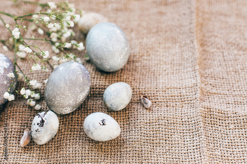 Stylish Easter eggs with spring flowers on rustic fabric in sunny light on wood. Modern colorful eggs painted with natural dye in grey marble. Happy Easter, greeting card