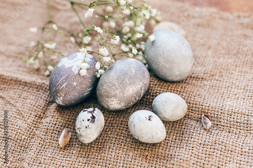 Stylish Easter eggs with spring flowers on rustic fabric in sunny light on wood. Modern colorful eggs painted with natural dye in grey marble. Happy Easter, greeting card