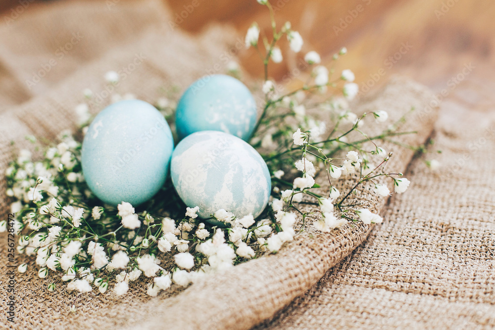 Stylish Easter eggs with spring flowers in floral nest on rustic fabric in sunny light on wood. Modern colorful eggs painted with natural dye in blue marble. Happy Easter, greeting card Stylish Easter eggs with spring flowers in floral nest on rustic fabric in sunny light on wood. Modern colorful eggs painted with natural dye in blue marble. Happy Easter, greeting card