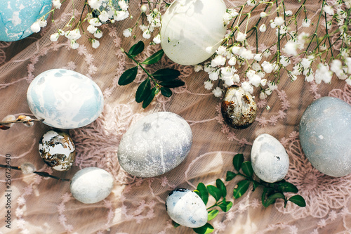 Stylish Easter eggs flat lay with spring flowers and willow branches on rustic fabric in sunny light on wood. Modern colorful eggs painted with natural dye. Happy Easter, seasons greetings