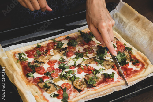 Woman cutting by knife rectangular shape and thick hand made romana's pizza traditional italian pizza margherita closeup