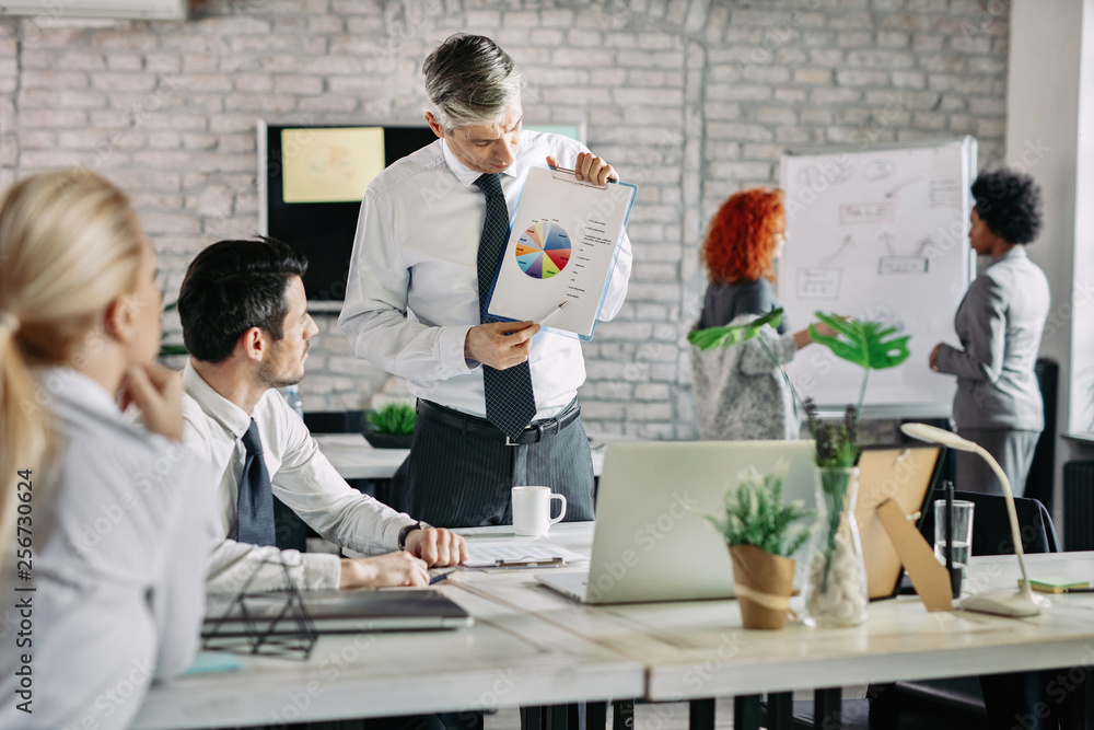 Businessman showing to his colleagues business report on a meeting in the office Businessman showing to his colleagues business report on a meeting in the office