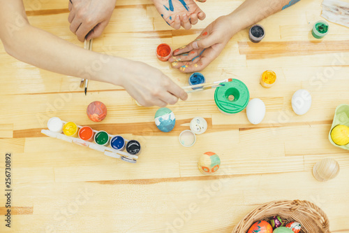 Cropped hands of happy family making various designs on eggs during Easter. Hands are spotted in paint.