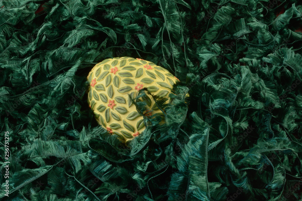 Yellow and green Easter egg in grass nest of green ribbon yarn Yellow and green Easter egg in grass nest of green ribbon yarn