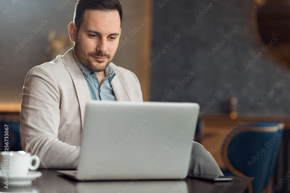 Serious businessman reading an e-mail on a computer while having coffee break in a cafe Serious businessman reading an e-mail on a computer while having coffee break in a cafe