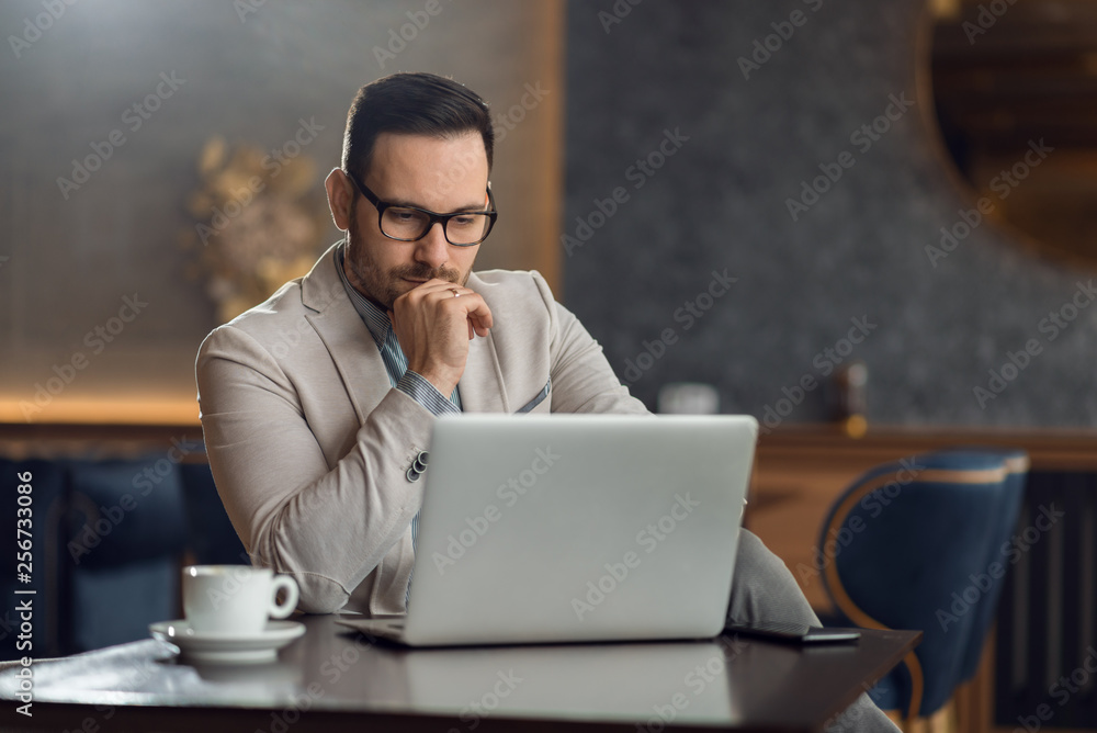 Pensive young businessman thinking while using laptop in a cafe Pensive young businessman thinking while using laptop in a cafe