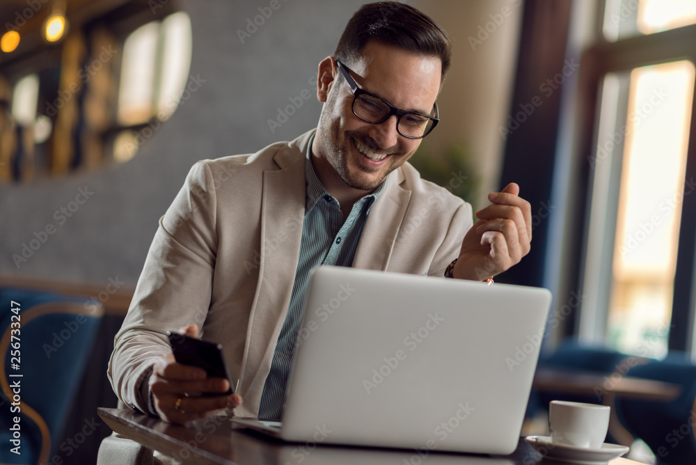 Happy young businessman reading an e-mail on laptop in a cafe Happy young businessman reading an e-mail on laptop in a cafe
