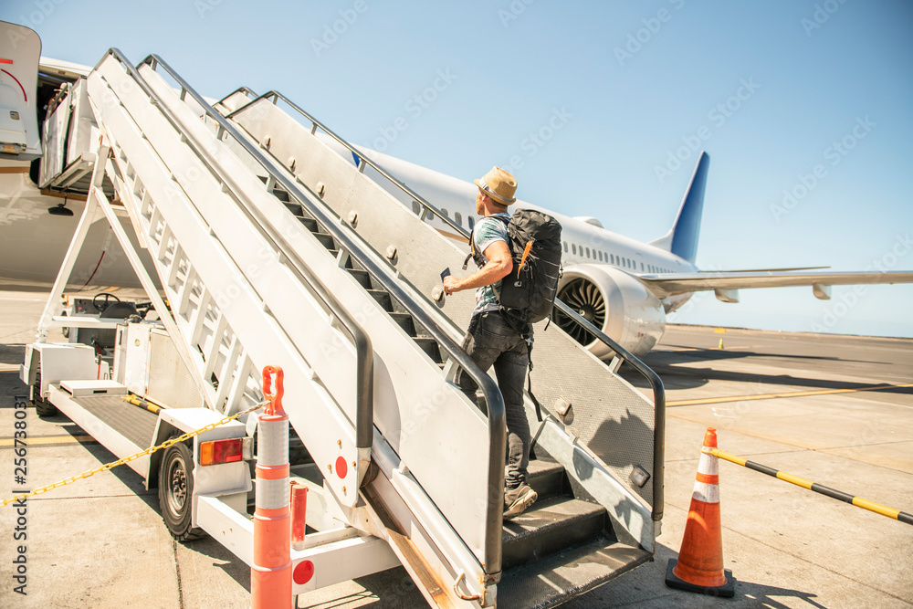 Naklejka premium A Young traveling man get in the plane with passport on the landing strip