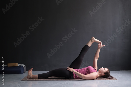 Woman doing Yoga asana Supta padangusthasana or reclining hand to big toe pose