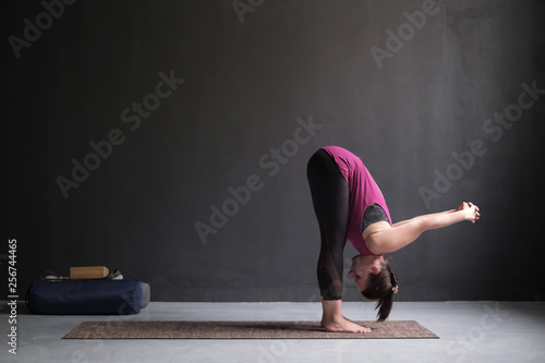 Sporty woman practicing yoga, standing forward bend exercise, uttanasana pose.