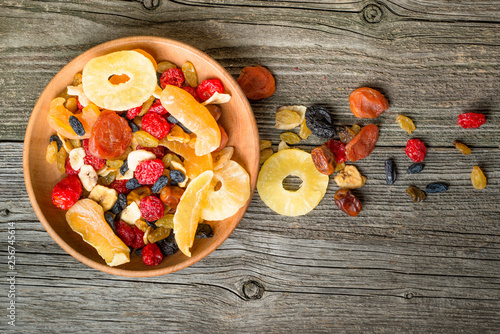 Mix of dried and candied fruit in bowl on a wooden background, top view