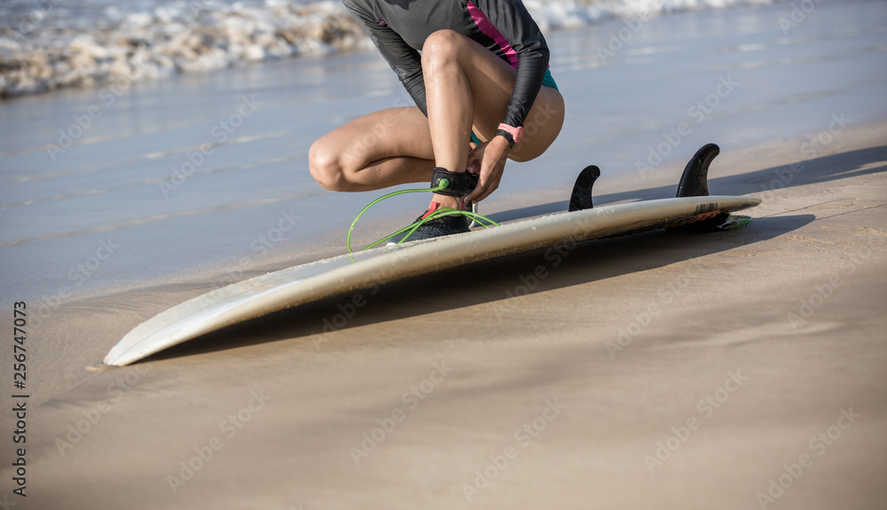 Naklejka premium female surfer fastening leash across leg before going to surf