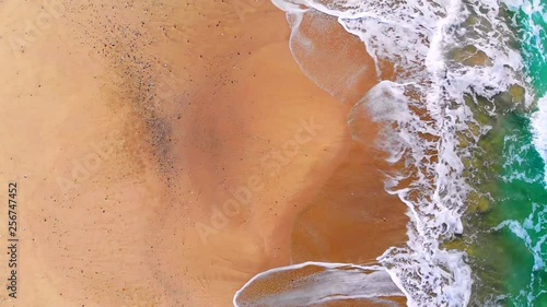 UHD 4K Vertical aerial drone view of splashing waves on multicolored beach