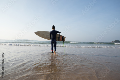 Woman surfer walking on the beach going to surf