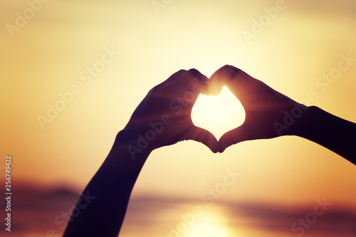 Hands in the shape of heart against the sunset over the sea.
