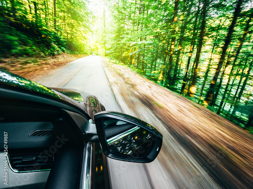 new modern car driving fast into forest with tall trees and empty mountain highway escaping running evading from all concept concept
