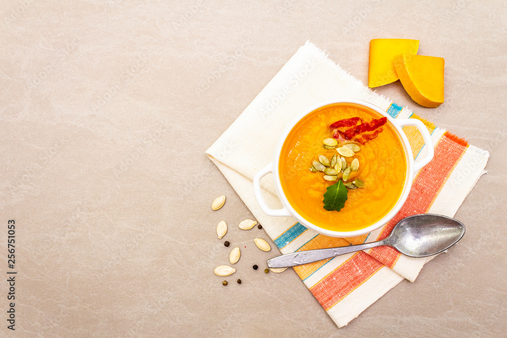 Pumpkin cream soup. White ceramic bowl with fresh pumpkin, dry seeds, smoked bacon. With vintage linen cloth (napkin) on stone background, top view Pumpkin cream soup. White ceramic bowl with fresh pumpkin, dry seeds, smoked bacon. With vintage linen cloth (napkin) on stone background, top view