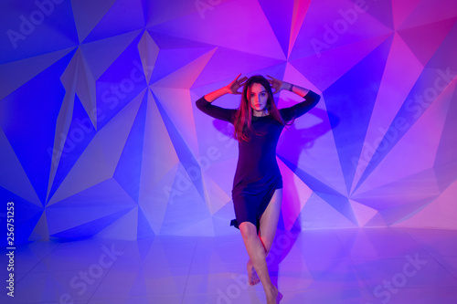Woman dancing on the background of a beautiful multicolored wall. Sexy slim lonely girl with long black hair in a beautiful dark blue dress. female holds her head. bright colorful geometry background 