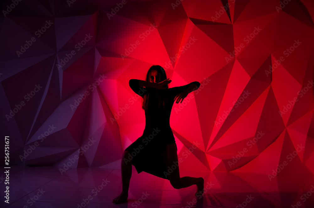 Woman dancing on the background of a beautiful multicolored wall. Sexy slim lonely girl with long black hair in a beautiful dark blue dress. covered her face with her hands. bright colorful geometry